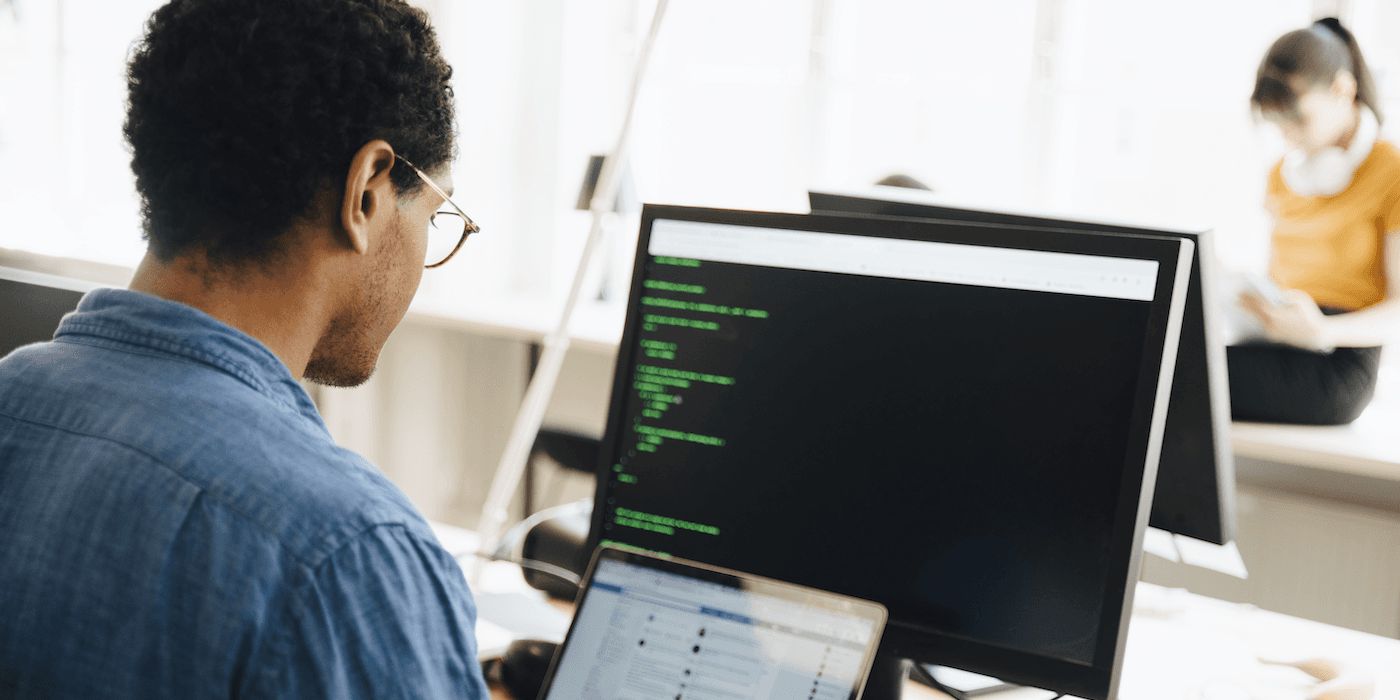 person sitting in front of a laptop and monitor writing code